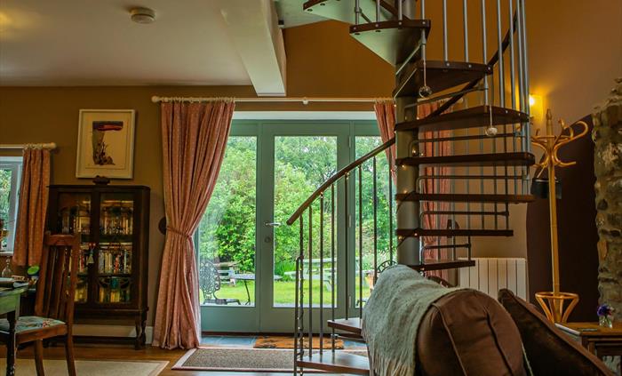 Hen Ffermdy cottage open plan living-dining area with spiral staircase to mezzanine bedroom and French window overlooking the gardens